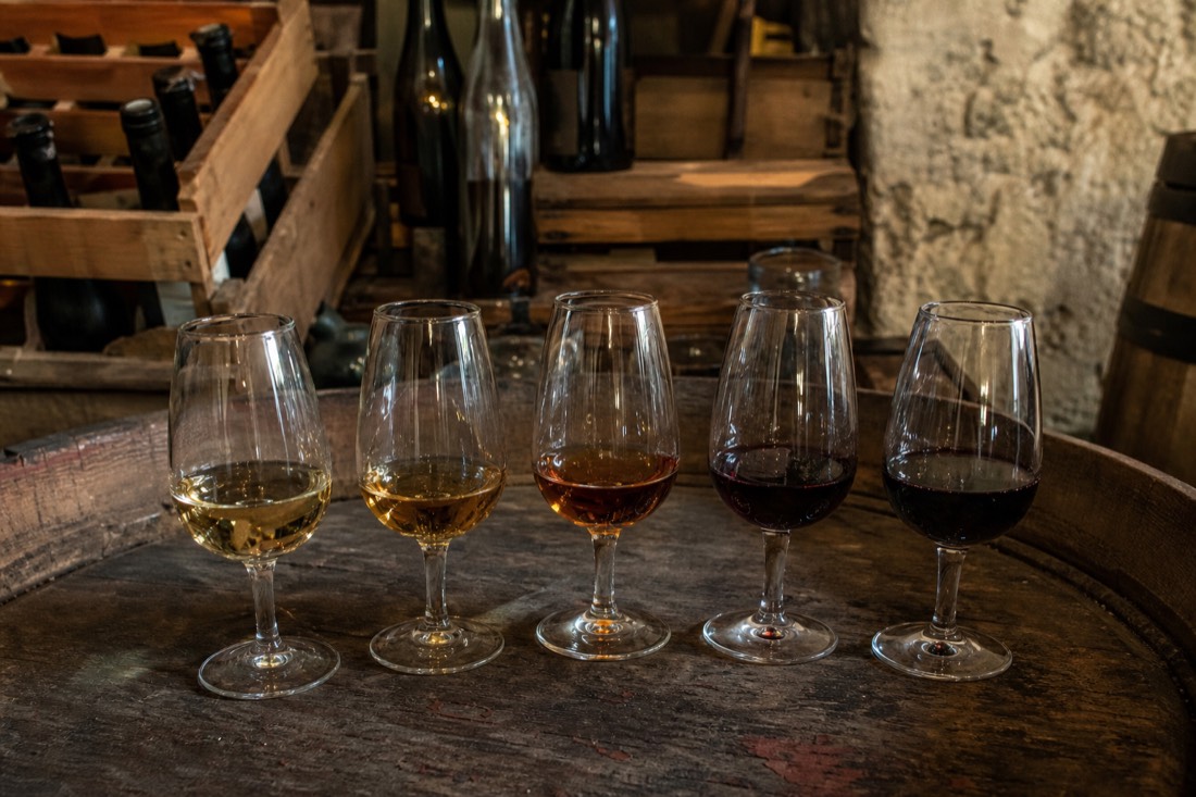 A flight of five wine glasses on a barrel top ranging from pale white port to deep red Douro wine