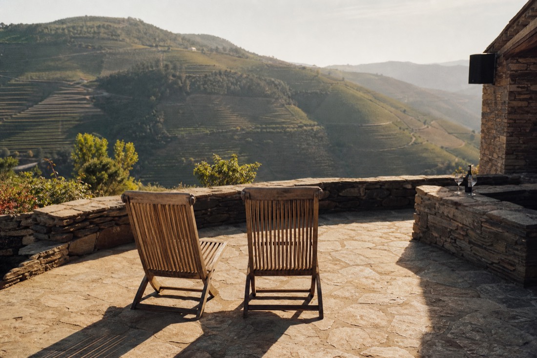 Two empty chairs facing terraced Douro vineyards in soft evening light