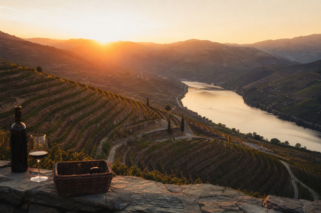 Amber sunset light flooding across layered vineyard terraces and the winding Douro River