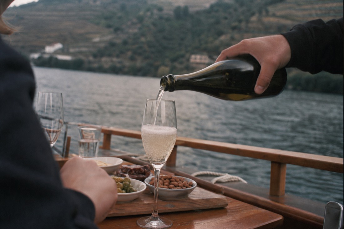 Sparkling wine being poured aboard a wooden boat on the Douro River with tapas plates alongside
