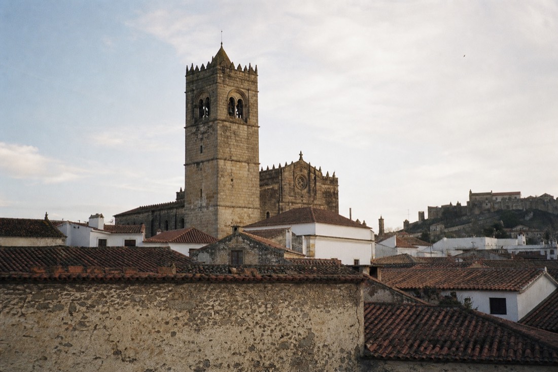 Old stone cathedral with a square Romanesque bell tower rising above the tiled roofs of a small Portuguese town