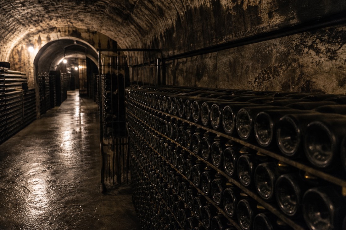 Dim underground cellar tunnel lined with racks of sparkling wine bottles aging on their sides