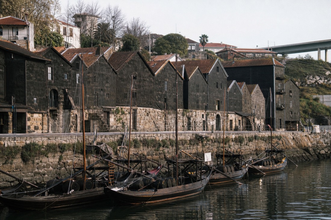Row of old dark-roofed wine lodges climbing the riverbank with rabelo boats moored on the water in front