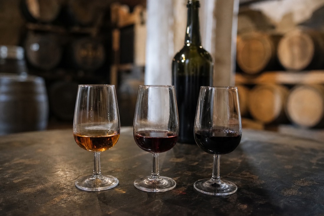Three glasses of Port in a tasting flight, from pale tawny to deep ruby, set on a cellar table
