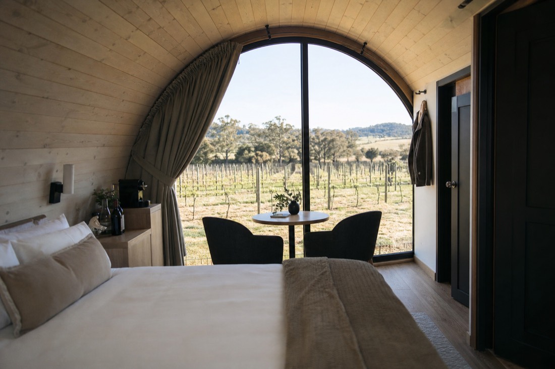 Interior of a barrel-shaped suite with curved timber ceiling and a window onto vineyard rows