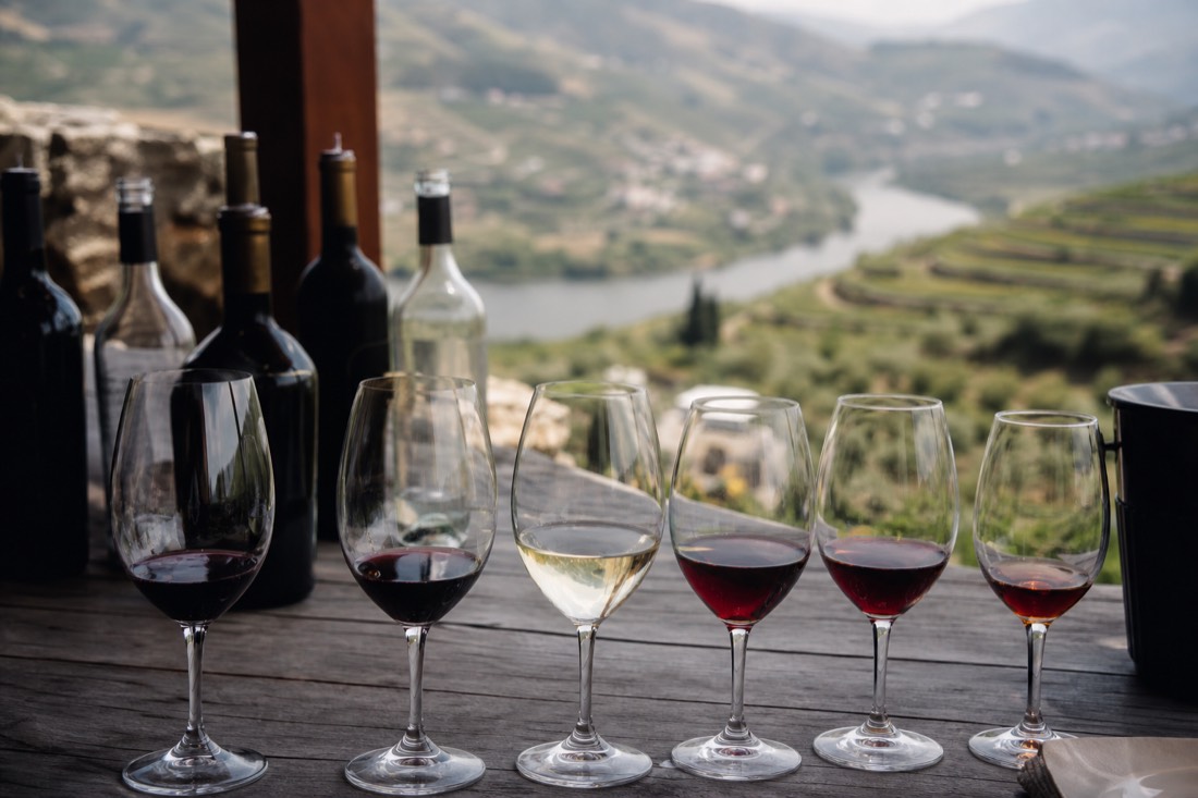 Row of wine glasses on a wooden table on a terrace overlooking terraced vineyards and the river