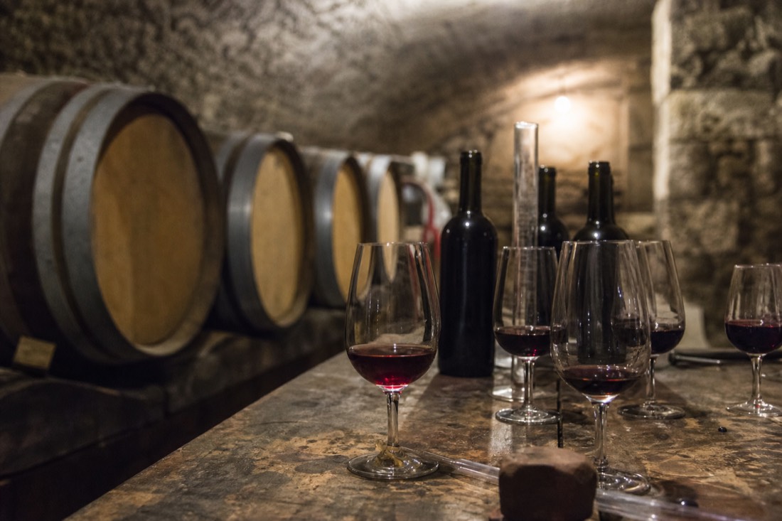Old stone wine cellar with rows of barrels and tasting glasses on a worn wooden table