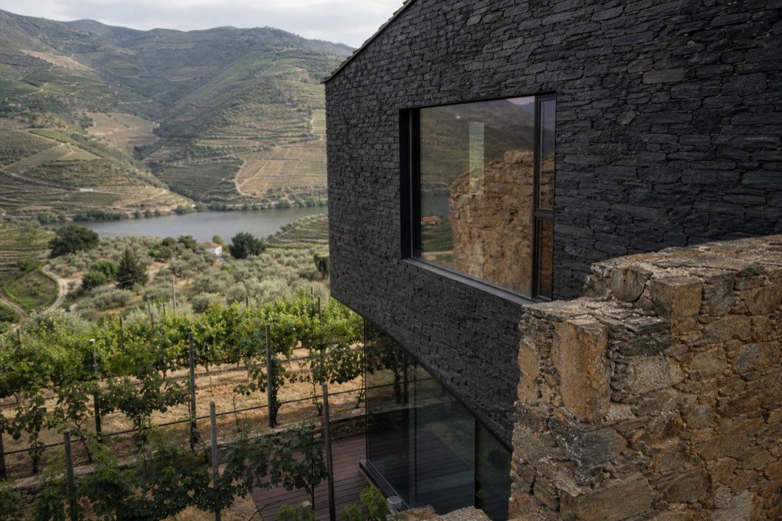 Modern slate-faced building with large glass windows beside old stone walls and vineyards in the Douro
