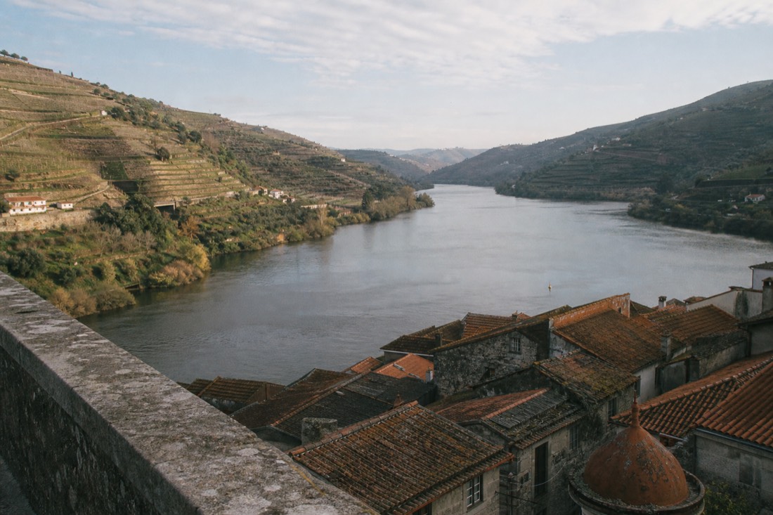 Split scene of city rooftops and distant vineyard terraces along the same river, the choice of where to sleep