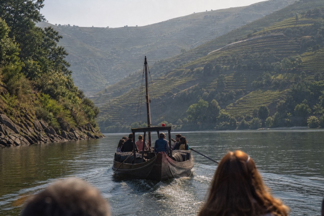 Wooden rabelo-style boat cruising the Douro River between terraced vineyard slopes near Pinhão